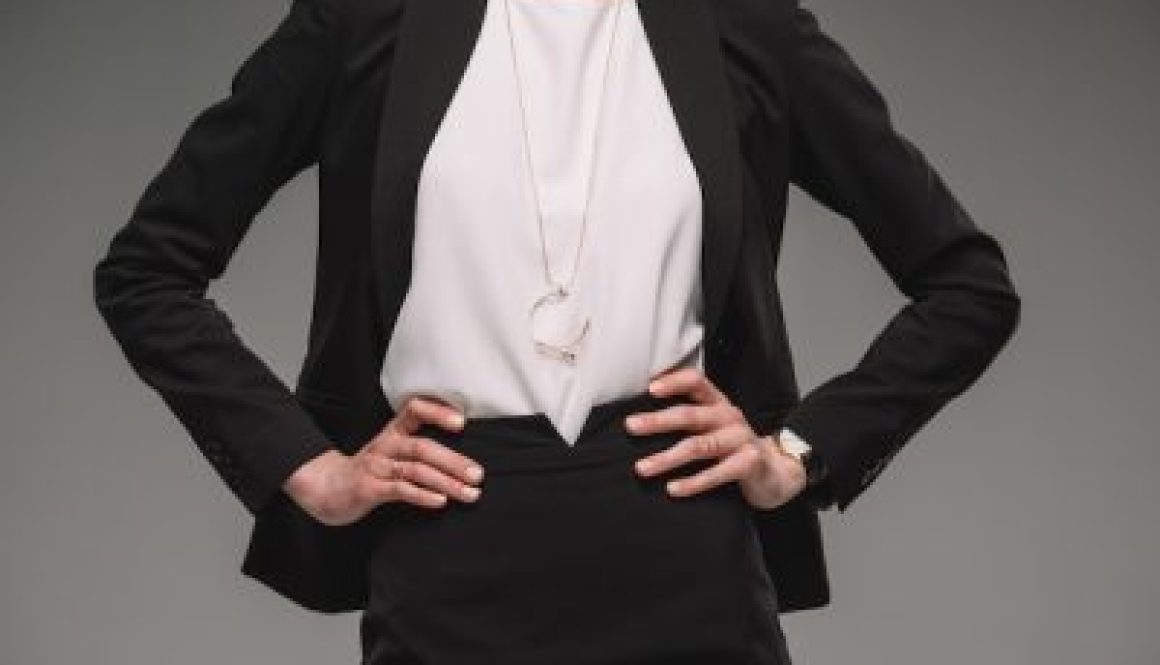 cropped image of businesswoman standing with hands on hips isolated on grey background