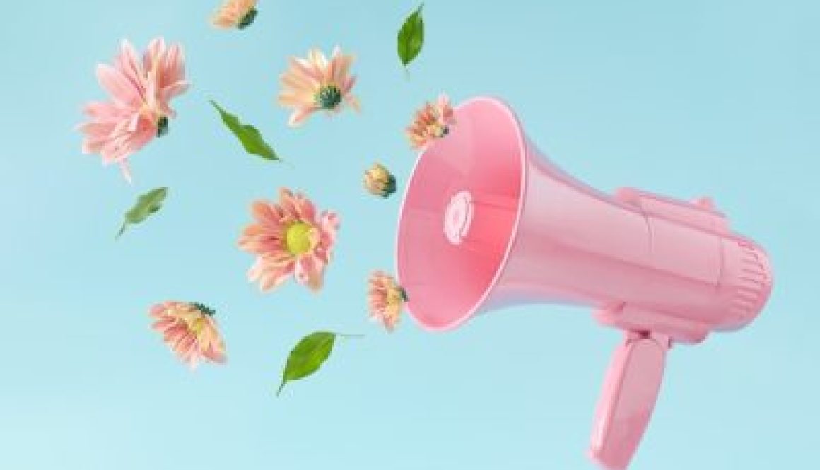 Pink megaphone with colorful summer flowers and green leaves against pastel blue background. Advertisement idea. Minimal nature concept.